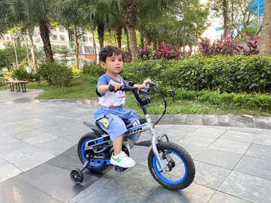 Bé trai tập trung điều khiển xe đạp với bánh phụ hỗ trợ