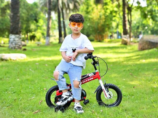 Bé trai thư giãn bên chiếc xe đạp sau khi đạp xe giữ công viên